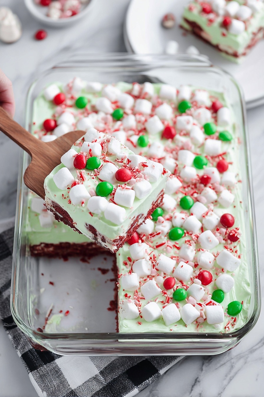 A close-up view of a slice of cake being held above a white marbled surface, showing four distinct layers: the bottom layer is deep red and moist with a soft, porous texture; above that is a thick pale cream layer embedded with small sections of the red cake; the third layer is a smooth light green frosting topped with small red sprinkles; and the top is decorated with mini white marshmallows and round candy pieces in red and green, with the whole cake visible in the background on a white marbled surface. Photo taken with an iphone --ar 2:3 --v 7 - Red Velvet Poke Cake with Cheesecake Fluff, Festive Red Velvet Cake, Cheesecake Fluff Dessert, Holiday Poke Cake, Easy Red Velvet Cake Recipe