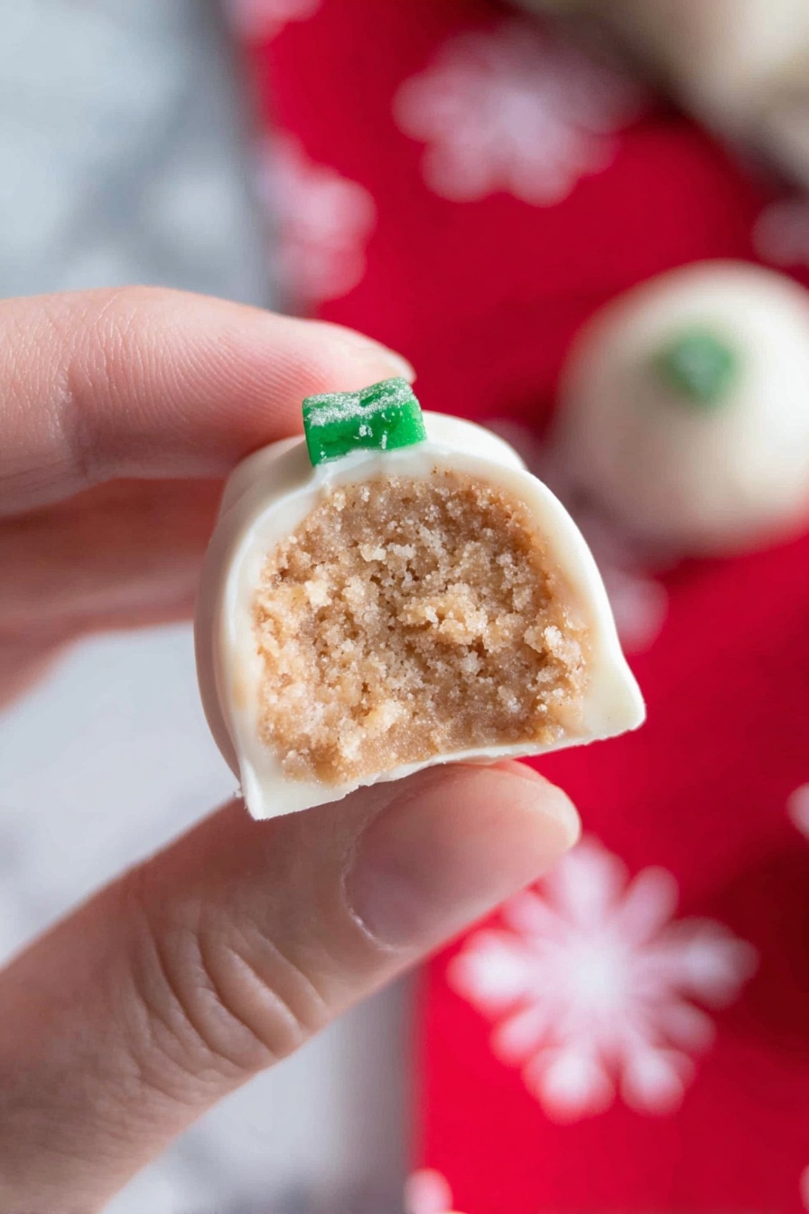 A white rectangular plate holds ten small round treats covered in smooth white icing, each topped with two small green holly leaves and one red berry decoration. The plate sits on a festive red cloth patterned with large white snowflakes. Around the plate, a few more of the same decorated treats and green and red holly leaf decorations are scattered on the white marbled surface. Photo taken with an iphone --ar 2:3 --v 7 - Snickerdoodle Cookie Dough Truffles, Cinnamon Cookie Dough Truffles, No-Bake Cookie Truffles, Cinnamon Dessert Bites, Easy Cookie Dough Truffles