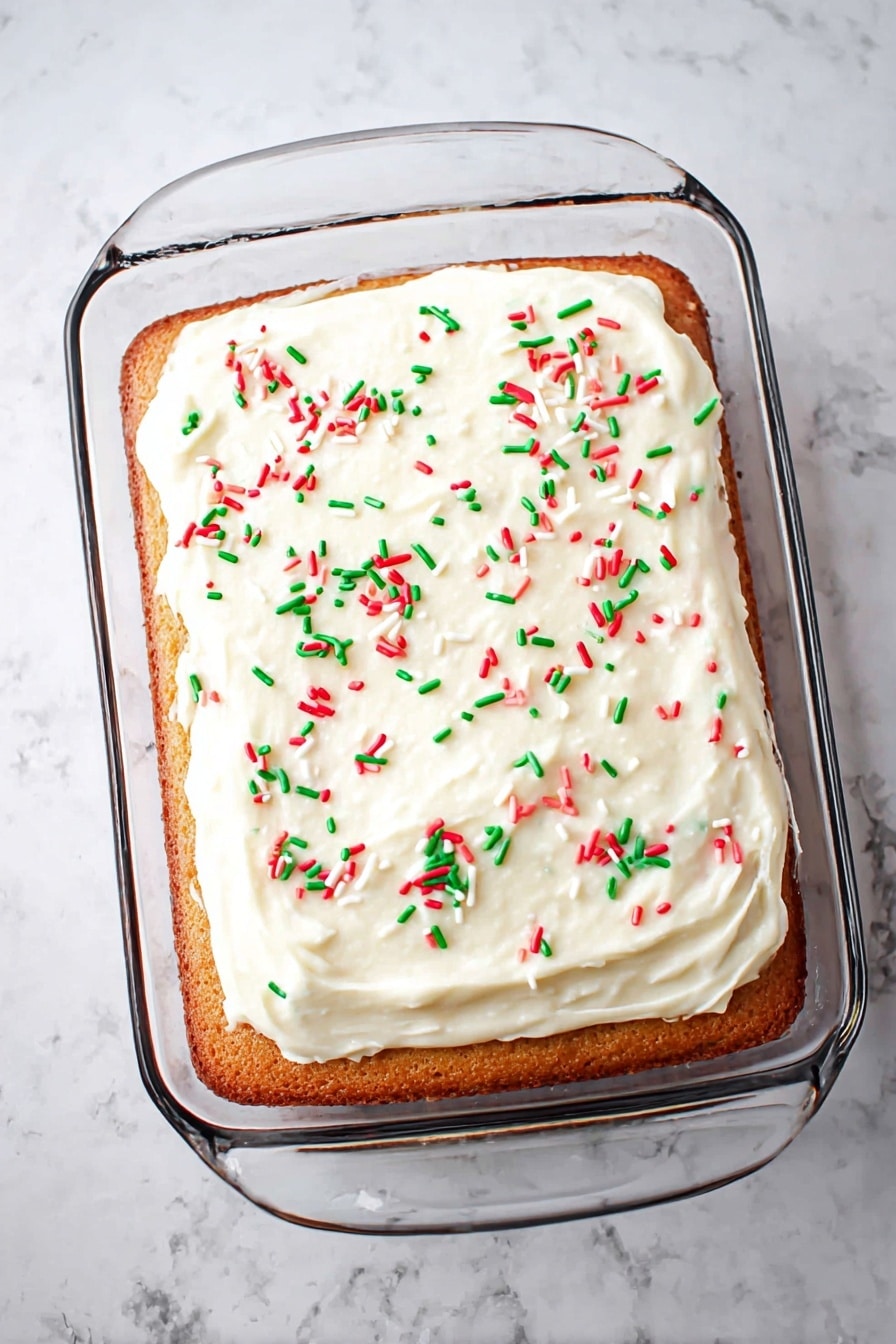 A single-layer rectangular cake in a clear glass baking dish sits on a white marbled surface. The cake is golden brown and topped evenly with smooth white frosting, which has a slightly creamy texture. Scattered across the top are small, thin sprinkles in red, green, and white, adding a festive touch. The clear dish's handles are visible on the sides, and the overall look is clean and simple. photo taken with an iphone --ar 2:3 --v 7 - Festive Jello Poke Cake, easy holiday dessert, colorful jello cake, party dessert recipes, no-bake jello cake