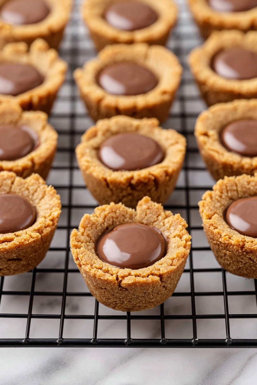 A pyramid stack of small round cookie cups filled with smooth, shiny milk chocolate sits on a white rectangular plate. Each treat has a thick, light brown crumbly cookie shell with a slightly rough texture, and a glossy chocolate center that looks creamy and soft. The cookies are evenly sized and closely packed, creating a pleasing, repetitive pattern of two layers—the cookie base forming the outer part and the chocolate sitting in the middle. The scene is bright with a white marbled texture in the background. photo taken with an iphone --ar 2:3 --v 7 - Peanut Butter Cup Cookies, peanut butter cookies, easy cookie recipes, quick dessert ideas, soft peanut butter cookies