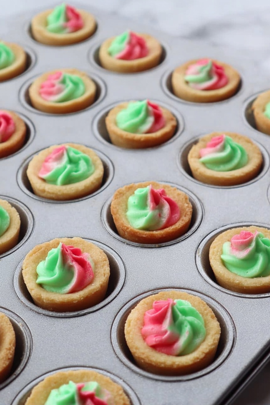 Three small round cupcakes sit on a white marbled surface covered with a light layer of Christmas-themed paper decorated with reindeer, trees, and gifts. Each cupcake has a soft, light golden-brown base with a smooth frosting swirl on top that mixes red and green colors in a gentle spiral pattern. The frosting appears creamy with a slight shine, neatly shaped in a small peak at the center of each cupcake. The overall look is festive and neat, suggesting a holiday theme. photo taken with an iphone --ar 2:3 --v 7 - Sugar Cookie Pudding Cups with Swirl Filling, festive dessert recipes, easy holiday desserts, colorful pudding dessert, no-bake cookie cups