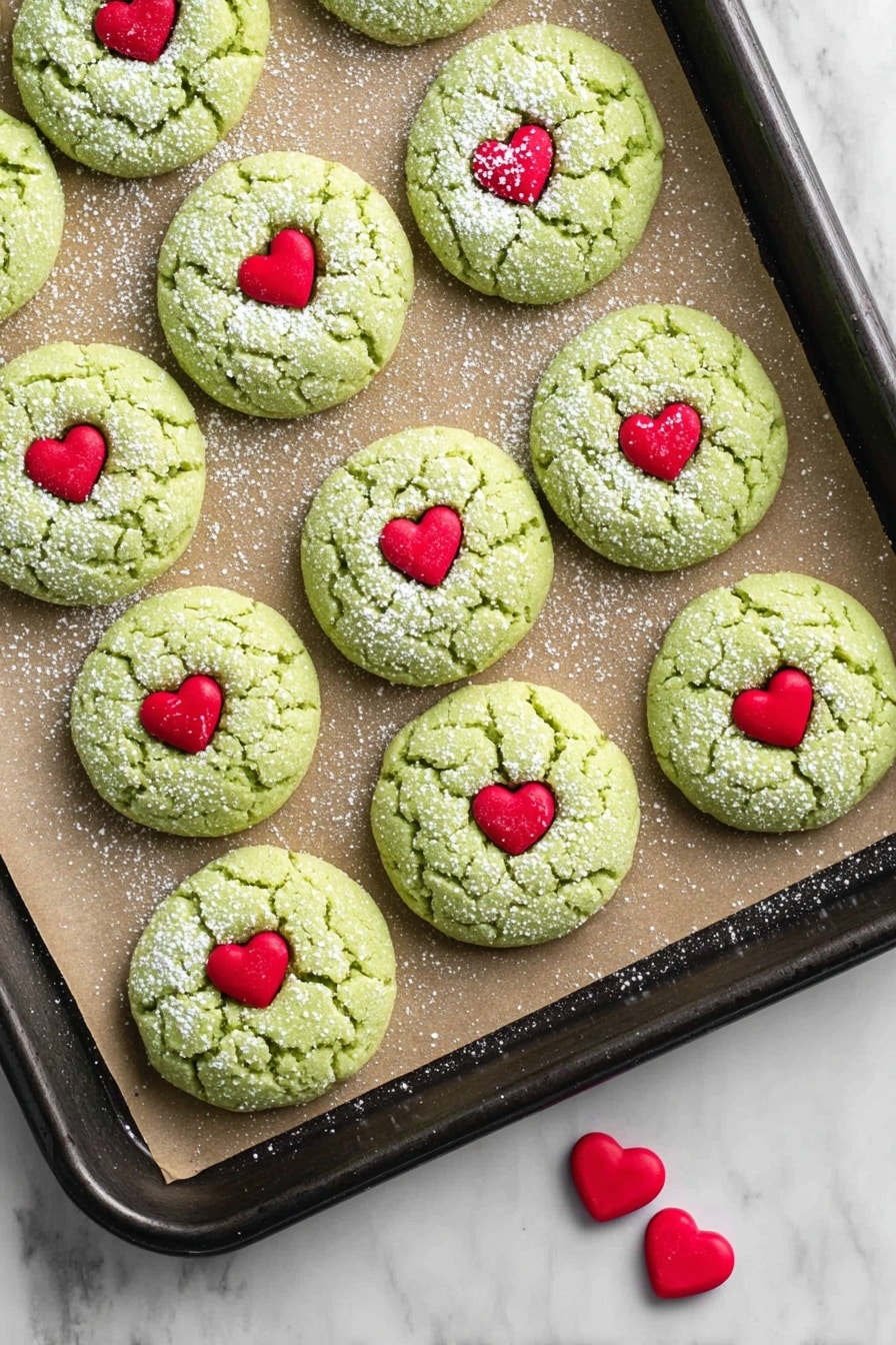 A stack of four light green cracked cookies with white powdered sugar dusting lays on a white marbled surface, each cookie topped with a small red heart candy in the center. Beside the stack, two more similar cookies lie flat, showing the same cracked texture and red heart candy centers. Behind the cookies, there is a clear glass bottle filled with white milk and a metal straw inside. On the left side, there is a green cloth with small white polka dots draped loosely. On the right side, there are red and dark red berry sprigs arranged casually. Photo taken with an iphone --ar 2:3 --v 7 - Grinch Heart Cake Mix Cookies, festive green cookies, easy holiday cookie recipe, adorable Christmas treats, soft cake mix cookies