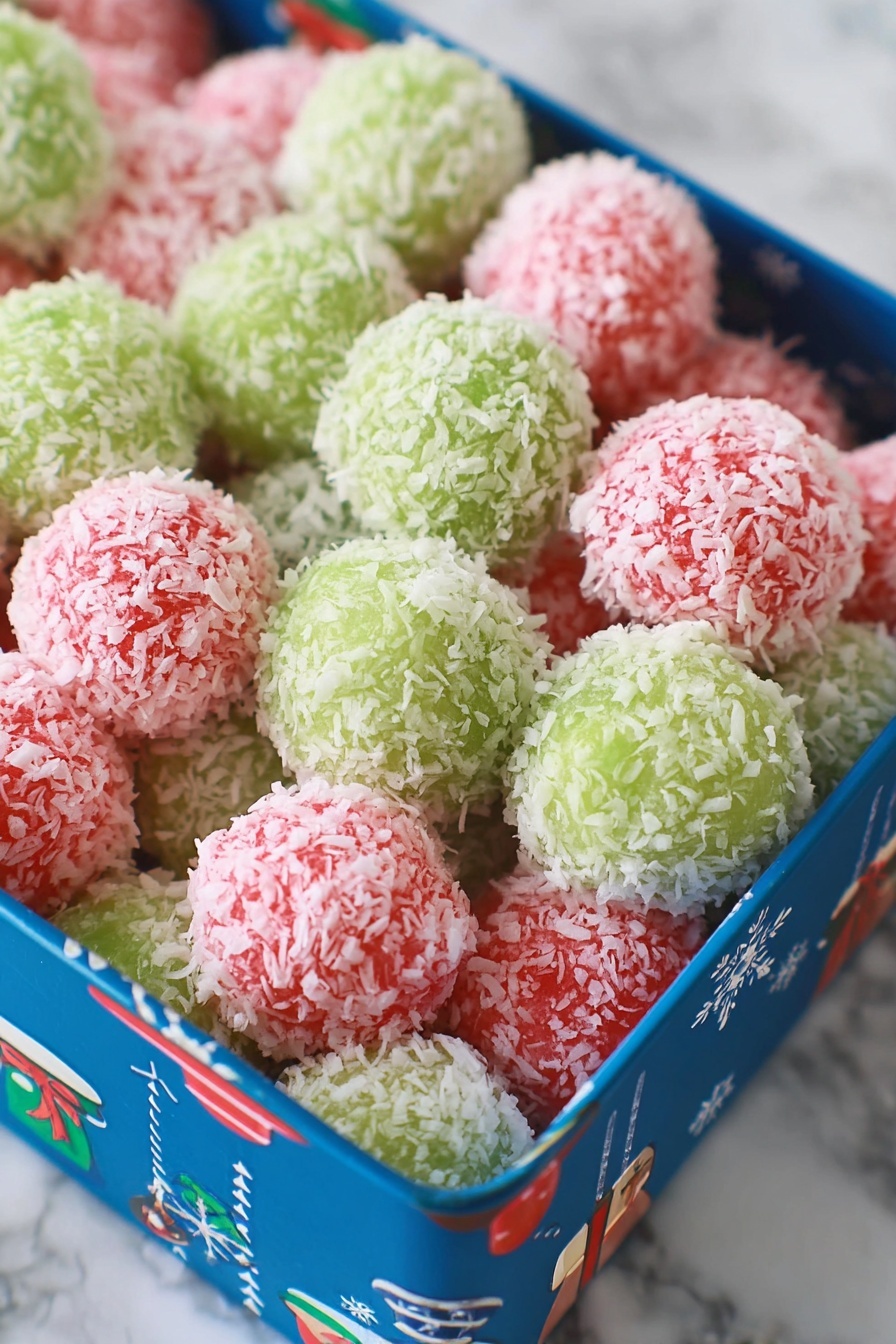 The image shows a white plate filled with small, round balls coated in shredded coconut. The balls are arranged in neat rows, with two colors visible: bright pink and light green. Each ball is fully covered with white coconut flakes, giving them a textured and fluffy appearance. The pink balls take up about two-thirds of the plate while the green balls fill the remaining third at the front. The plate is placed on a white marbled surface. photo taken with an iphone --ar 2:3 --v 7 - Festive Jello Coconut Balls, colorful holiday treats, no-bake coconut desserts, easy holiday snack, party appetizer ideas