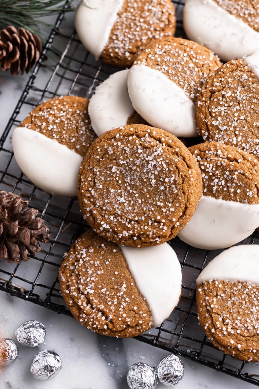 The image shows a close-up of two types of brown cookies with sparkling sugar crystals on top, arranged on a black cooling rack over a white marbled surface. Some cookies are half dipped in smooth, white icing covering one side, creating a two-tone look with the brown sugar crystals on the other half. Other cookies are ring-shaped with a striped, round chocolate candy placed in the center hole, featuring white and brown swirls. Small silver-wrapped candies and a pine cone are scattered around the cookies, adding a festive touch. Photo taken with an iphone --ar 2:3 --v 7 - Ginger Cookies with White Chocolate Dipping, spicy ginger cookies, holiday ginger cookies, chewy ginger cookies, white chocolate dipped cookies