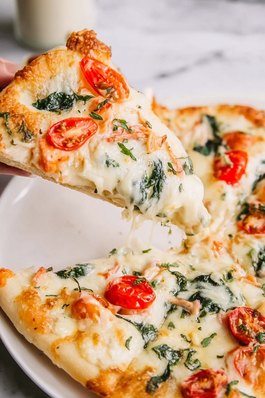 A rectangular pizza on a metal baking tray lined with parchment paper sits on a white marbled surface. The pizza has one thick dough layer with a golden brown edge. On top, there is a layer of melted white cheese covering the whole pizza, mixed with small shrimp pieces that are light pink and scattered evenly. There are halved red cherry tomatoes and chopped bright green spinach leaves spread across the top. Thin shreds of cheese are sprinkled lightly over the pizza, with a few browned spots where the cheese is toasted. In the upper right corner, a small white bowl of shredded cheese and a silver salt shaker are visible. Photo taken with an iphone --ar 2:3 --v 7 - Shrimp Alfredo Pizza, creamy shrimp pizza recipe, easy seafood pizza, homemade shrimp pizza, alfredo sauce pizza