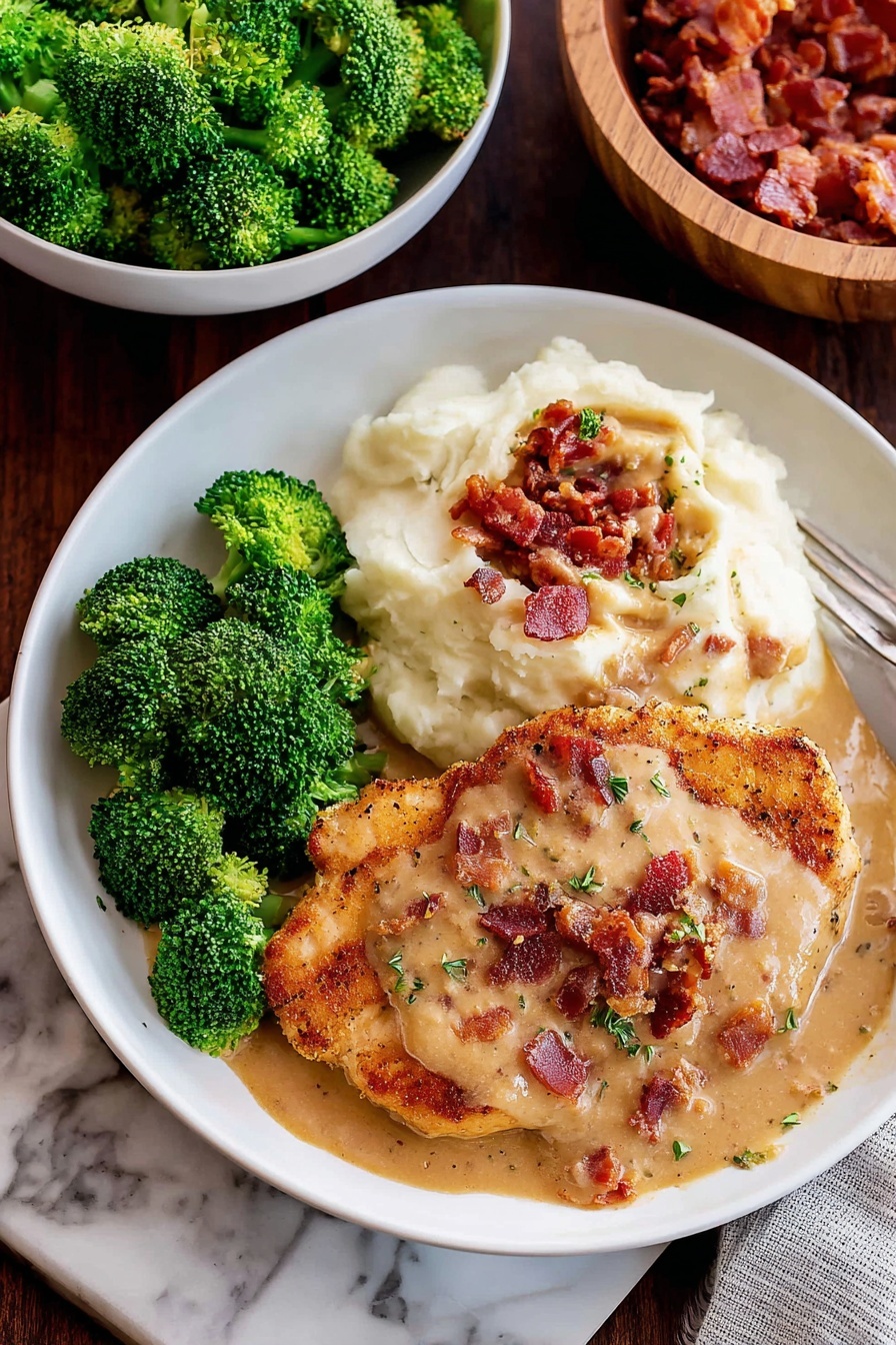 A white plate holds three main layers with a white marbled surface in the background: on the right side, a smooth, creamy white layer of mashed potatoes; in the middle, a golden brown fried chicken piece covered with beige gravy with small green herb bits and topped with small, crispy, reddish-brown bacon pieces; on the left side, bright green, tightly bunched broccoli florets. The colors contrast well, and the textures include smooth, crispy, and soft. The photo taken with an iphone --ar 2:3 --v 7 - Smothered Chicken with Bacon and Creamy Gravy, hearty chicken dinner, bacon chicken recipe, creamy gravy chicken, comfort food chicken dish