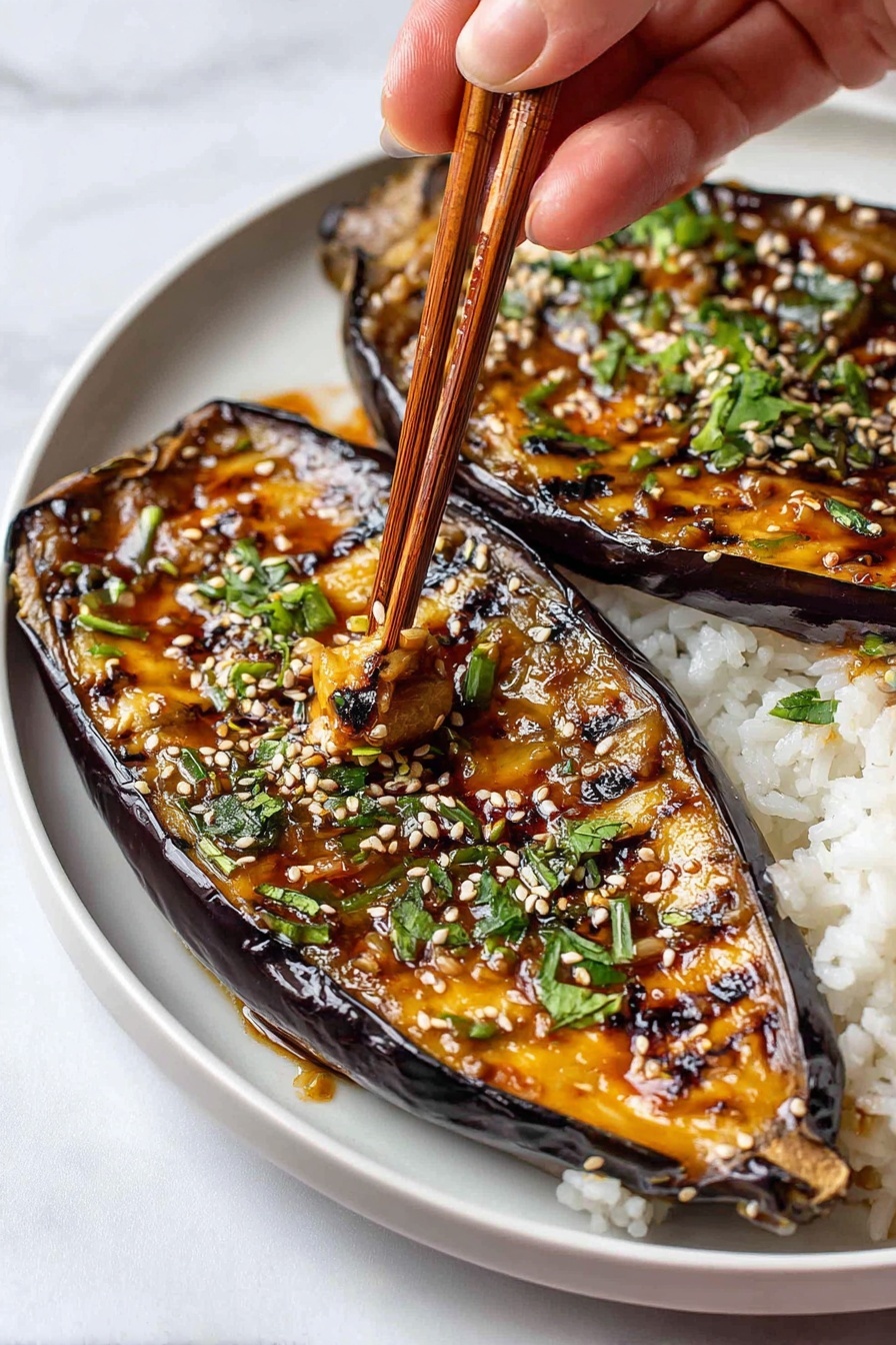The image shows two grilled eggplant halves placed on a bed of white rice on a white plate. The eggplants have a dark purple skin with a shiny, textured surface and grill marks across their soft, golden-orange flesh. Each half is topped with sesame seeds and chopped green herbs, adding a touch of white and green contrast. A woman's hand is using light brown wooden chopsticks to pick up a piece of the eggplant, revealing the soft inside covered in a glossy sauce. The background is a white marbled surface. photo taken with an iphone --ar 2:3 --v 7 - Miso Eggplant, Eggplant recipe, Umami vegetable dish, Easy Asian eggplant, Healthy eggplant appetizer