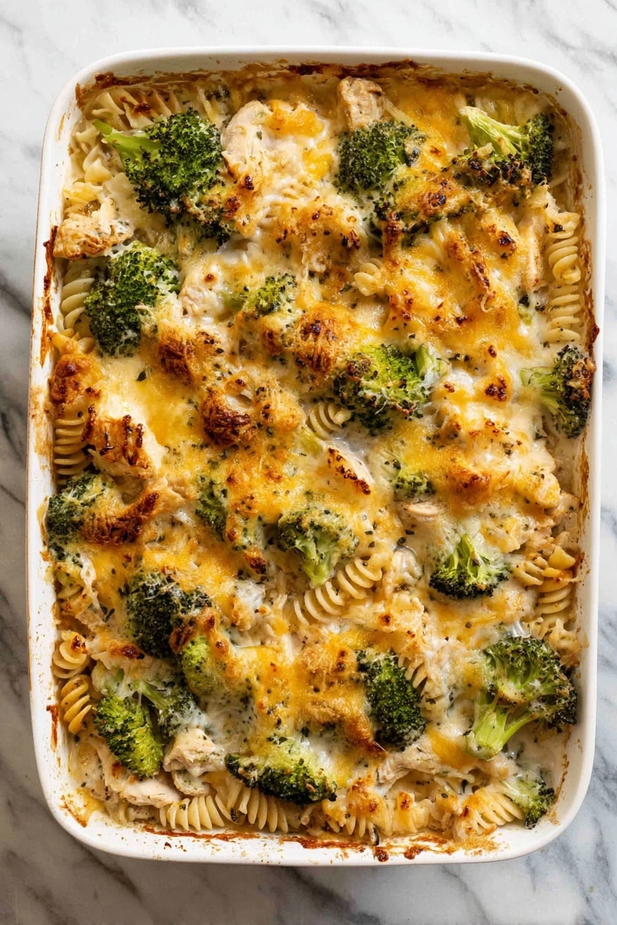 A white baking dish filled with a baked casserole showing three main layers: the bottom layer of pale yellow spiral pasta, the middle layer of green broccoli florets mixed evenly with pieces of light-colored cooked chicken, and the top layer features a golden-brown melted cheese crust with some darker toasted spots, giving it a slightly crispy texture. The edges of the dish show hints of bubbling sauce that has browned slightly, all sitting on a white marbled surface. photo taken with an iphone --ar 2:3 --v 7 - Creamy Chicken and Broccoli Pasta Bake, chicken broccoli pasta casserole, cheesy baked chicken and broccoli, easy chicken pasta bake, comforting pasta bake