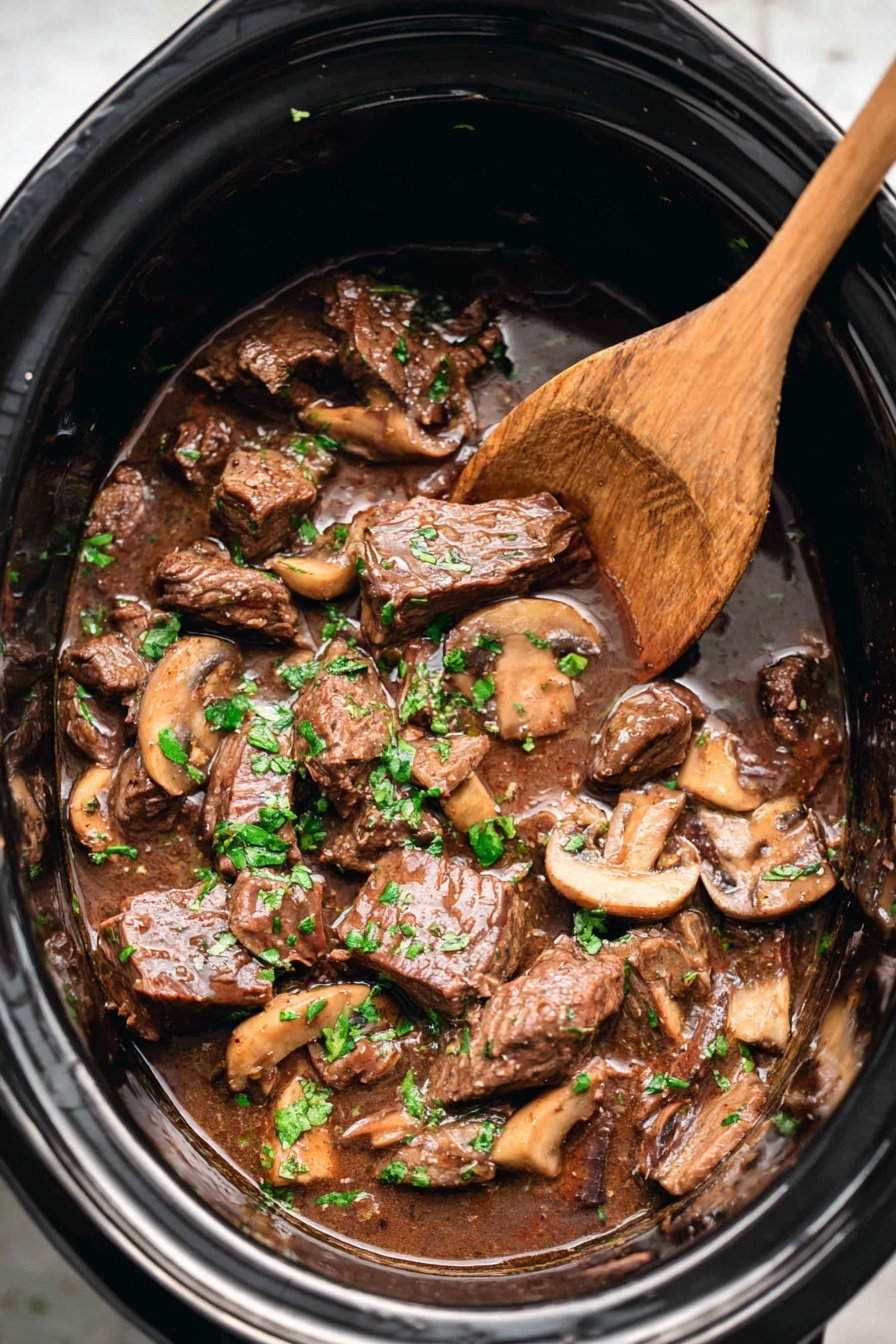 A white bowl filled with three layers: the bottom layer is wide, curly egg noodles in a pale yellow color, the middle layer consists of tender dark brown beef chunks mixed with sliced light brown mushrooms, and the top layer is sprinkled with bright green chopped parsley. A black spoon with a golden handle is placed on the right side inside the bowl, resting partly on the noodles and meat. The bowl is set on a white marbled surface with blurred green herbs and a blue and beige cloth in the background. Photo taken with an iphone --ar 2:3 --v 7 - Crockpot Steak and Mushroom Gravy, easy slow cooker steak recipe, hearty mushroom gravy dinner, tender crockpot beef and mushroom, comfort food steak recipes