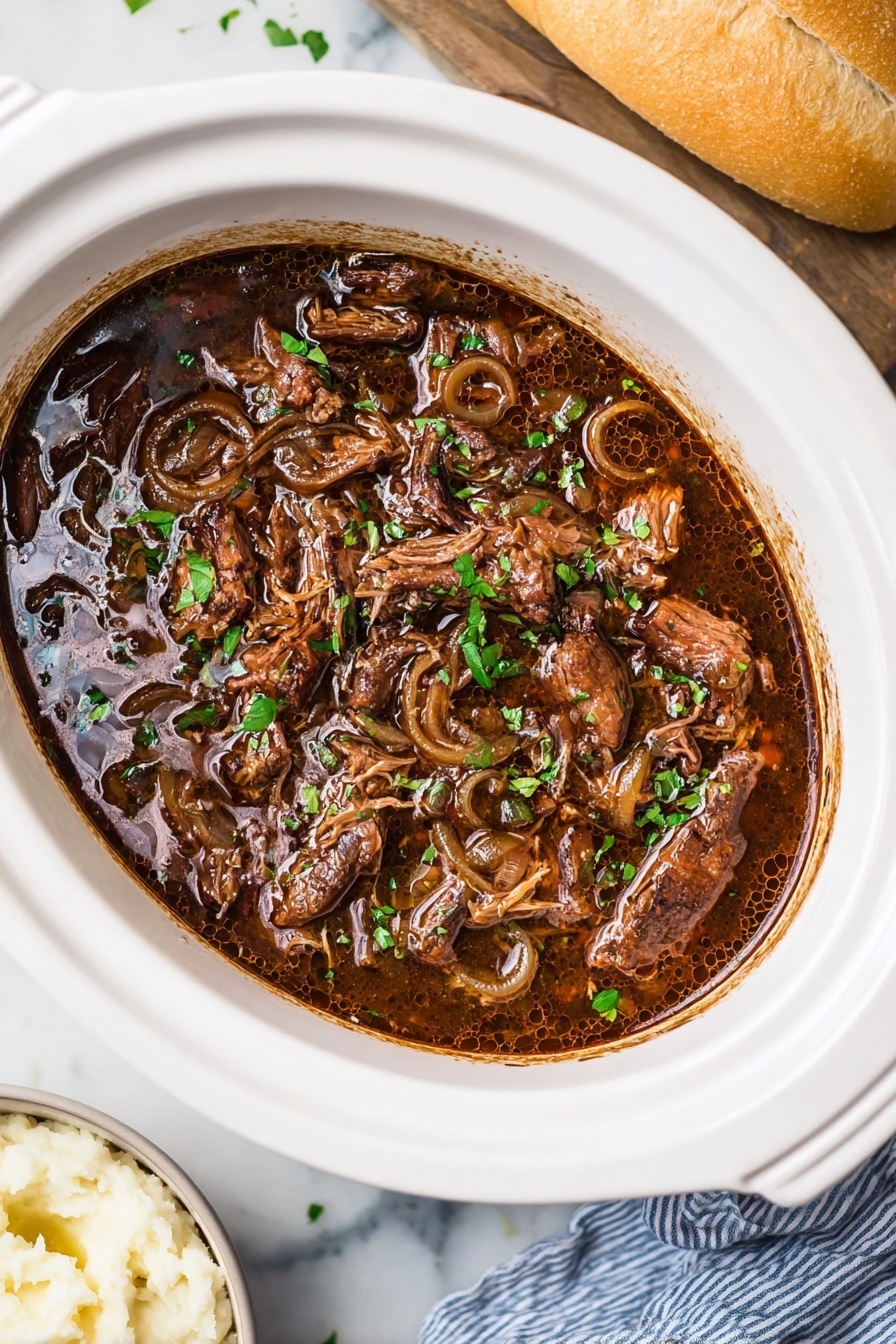 A slow cooker filled with a rich, dark brown stew shows multiple soft, tender pieces of shredded meat mixed with translucent, cooked onion rings. The stew has a glossy surface with small bubbles of oil scattered around. Fresh green chopped herbs are sprinkled on top, adding a pop of color. The white slow cooker sits on a white marbled surface, with a glimpse of a garlic bread and white bowl with mashed potatoes or a similar side dish on the side. A blue and white striped cloth napkin partially appears on the right side. Photo taken with an iphone --ar 2:3 --v 7 - Slow Cooker French Onion Roast, French Onion Roast, Easy French Onion Roast, Slow Cooker Roast Recipes, Comforting Dinner Recipes