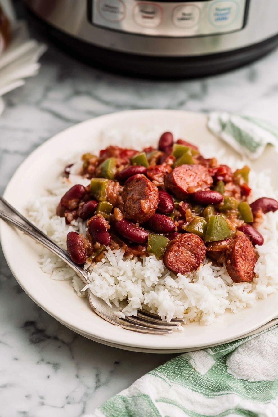 A white plate holds a bed of fluffy white rice topped with a mixture of cooked red kidney beans, chopped green bell peppers, and slices of browned sausage. The sausage pieces are thick and dark reddish-brown with a slight sheen, scattered among the glossy beans and vegetables. The rice grains look soft and slightly separated. A silver fork rests on the plate’s edge. The plate is on a white marbled texture surface, with a kitchen appliance visible in the background to the right and a white cloth with green stripes on the bottom right. Photo taken with an iphone --ar 2:3 --v 7 - Slow Cooker Red Beans and Rice, Easy Red Beans and Rice, Cajun Red Beans and Rice, Comfort Food Recipes, Make-Ahead Dinner Ideas