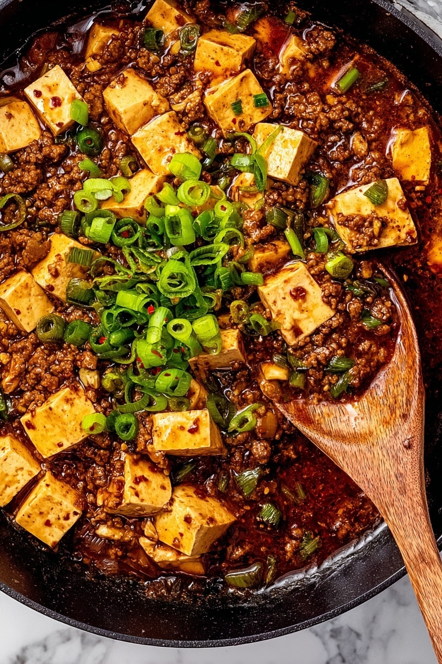 In a white bowl sitting on a white marbled surface, a dish shows two main layers. The bottom layer is fluffy white rice, filling the bowl. On top is a rich, brown minced meat sauce mixed with soft, light yellow tofu cubes, scattered unevenly. Bright green chopped spring onions are sprinkled over the top, adding fresh color. A gold spoon with a black handle is dipped into the dish near the edge of the bowl. The background includes a soft gray cloth slightly blurred. Photo taken with an iphone --ar 2:3 --v 7 - Mapo Tofu, Mapo Tofu recipe, spicy Chinese tofu, Chinese spicy tofu dish, Szechuan Mapo Tofu