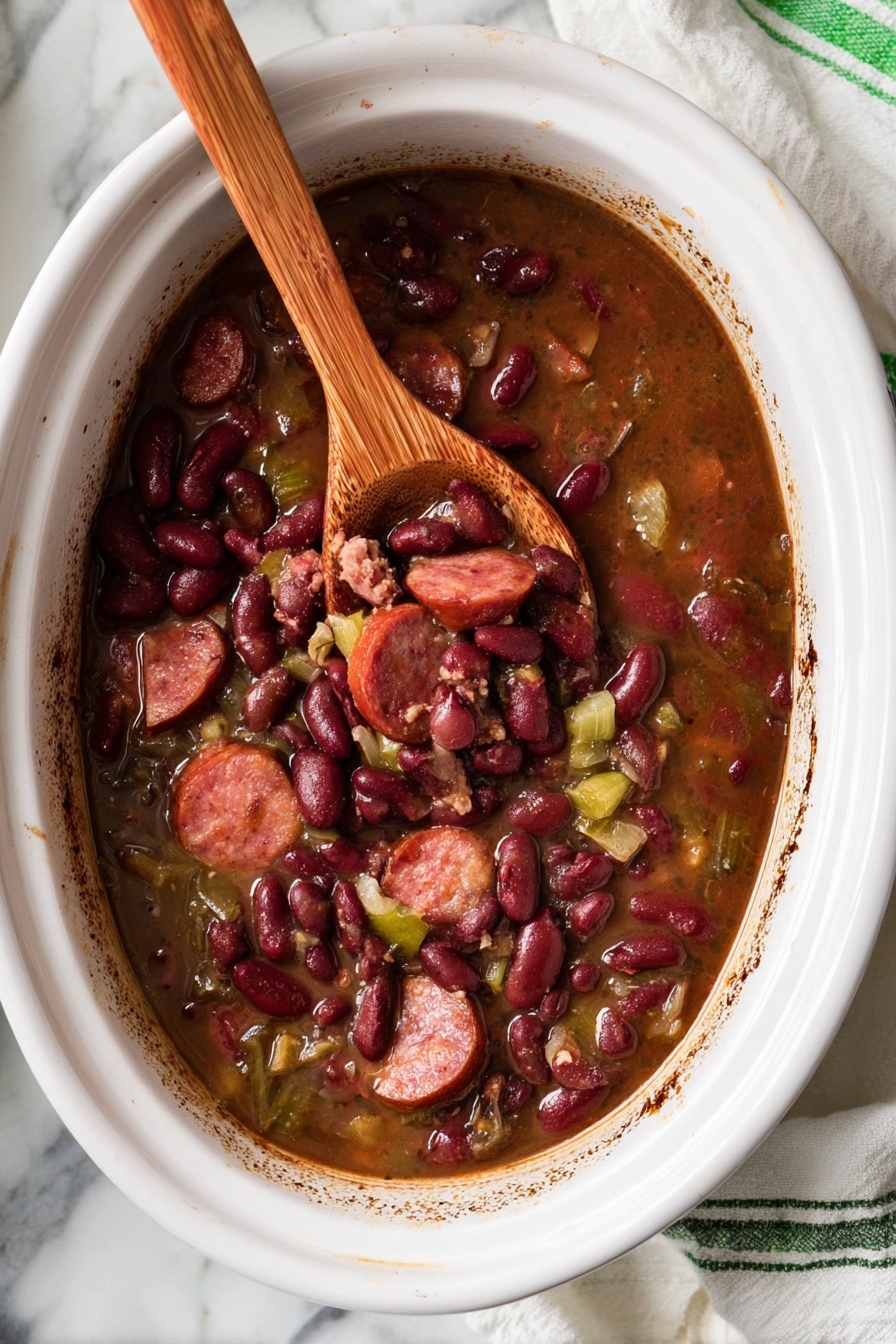 A white oval dish holds a warm stew made of dark red kidney beans, sliced sausage pieces, and small chunks of light green vegetables mixed in a rich brown broth. A wooden spoon rests inside the dish, lifting a scoopful of the stew, showing the beans and sausage clearly. The dish’s edges have some browned marks from cooking. The setting includes a white marbled surface with part of a white cloth with green stripes partly visible at the bottom right. Photo taken with an iphone --ar 2:3 --v 7 - Slow Cooker Red Beans and Rice, Easy Red Beans and Rice, Cajun Red Beans and Rice, Comfort Food Recipes, Make-Ahead Dinner Ideas