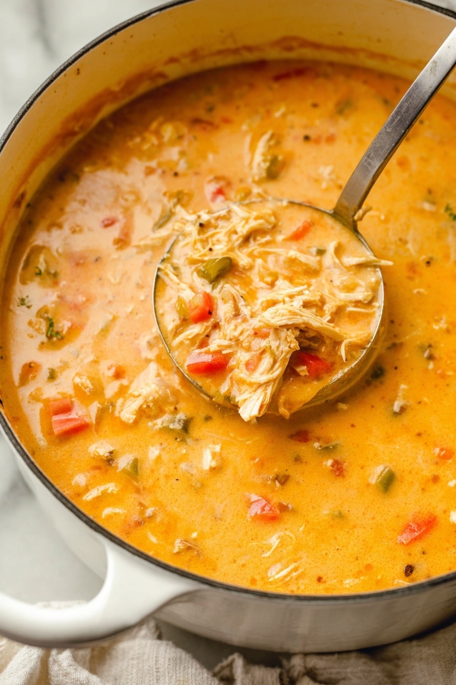 A close-up view of a thick creamy orange soup with visible pieces of shredded chicken, small chunks of red and green bell peppers, and some softer vegetable bits. The soup is inside a white pot with a curved white handle, resting on a white marbled surface partly covered with a cloth. A metal ladle is scooping up a portion of the soup, showing the mixed textures and colors clearly. photo taken with an iphone --ar 2:3 --v 7 - Creamy Buffalo Chicken Soup, spicy buffalo chicken soup, easy buffalo chicken soup, comforting chicken soup, creamy hot chicken soup